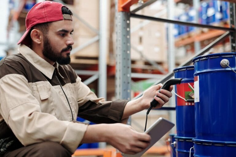 Male warehouse worker scanning barrels with a tablet for inventory management.
